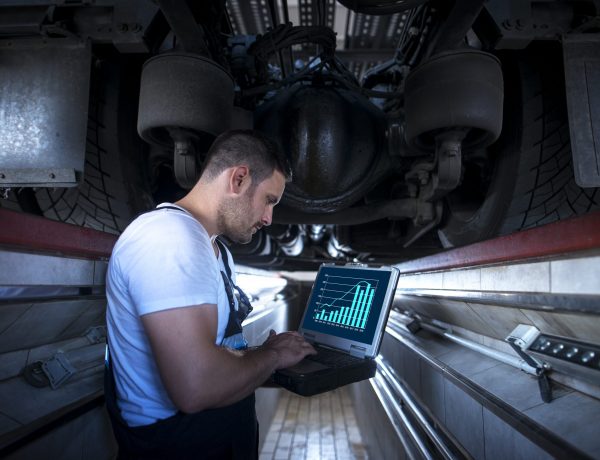 Vehicle mechanic with diagnostic tool laptop working under the truck in workshop.